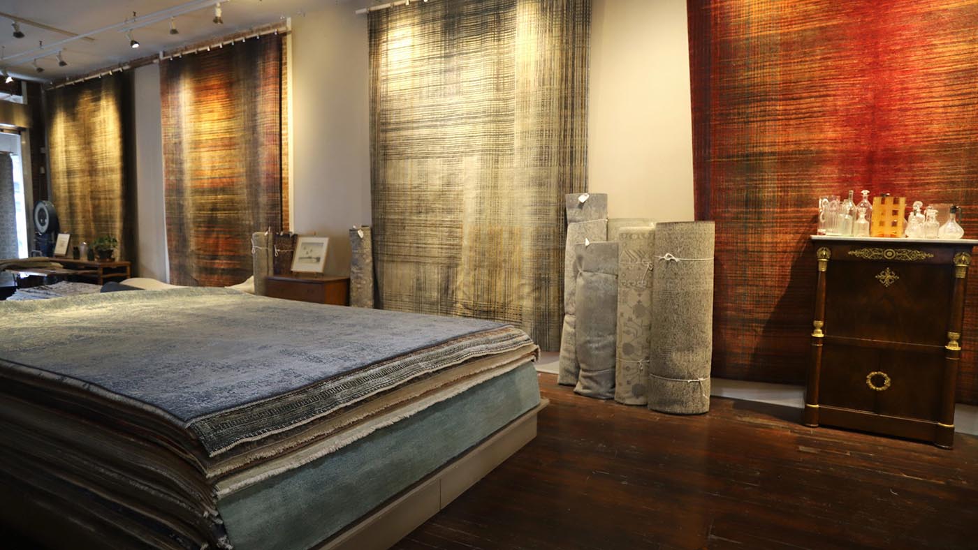 Rug showroom with rugs hung on walls, stacked flat, & rolled